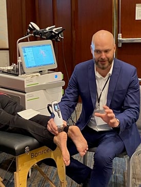 Dr. Hobrough demonstrating a handheld medical device on a patient's foot, accompanied by an advanced medical device.