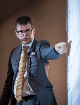 Dr. Knobloch presenting with a focused expression, pointing at a projection screen displaying technical details.