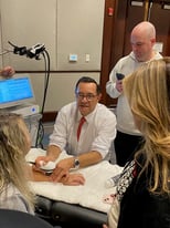 A demonstration of a medical device by Dr. Leal, showcasing its application on a patient’s arm while observers look on.