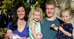 A smiling family of four, including a mother, father, and two children, standing outdoors.